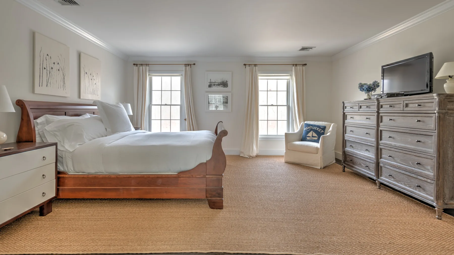 Un dormitorio con una cama de madera, dos ventanas y un sillón claro.