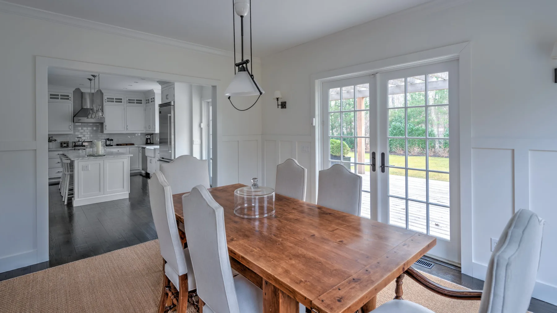 Un comedor con una mesa de madera junto a puertas de vidrio y una cocina al fondo.