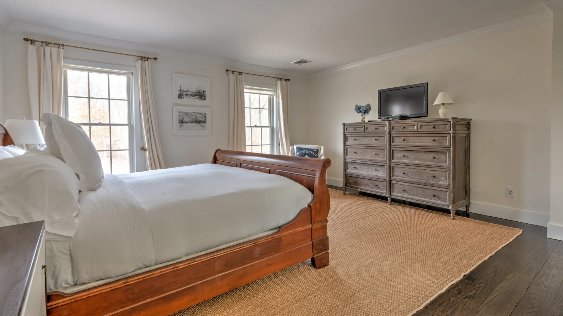 Dormitorio con una cama de madera, una cómoda y ventanas junto a una alfombra.