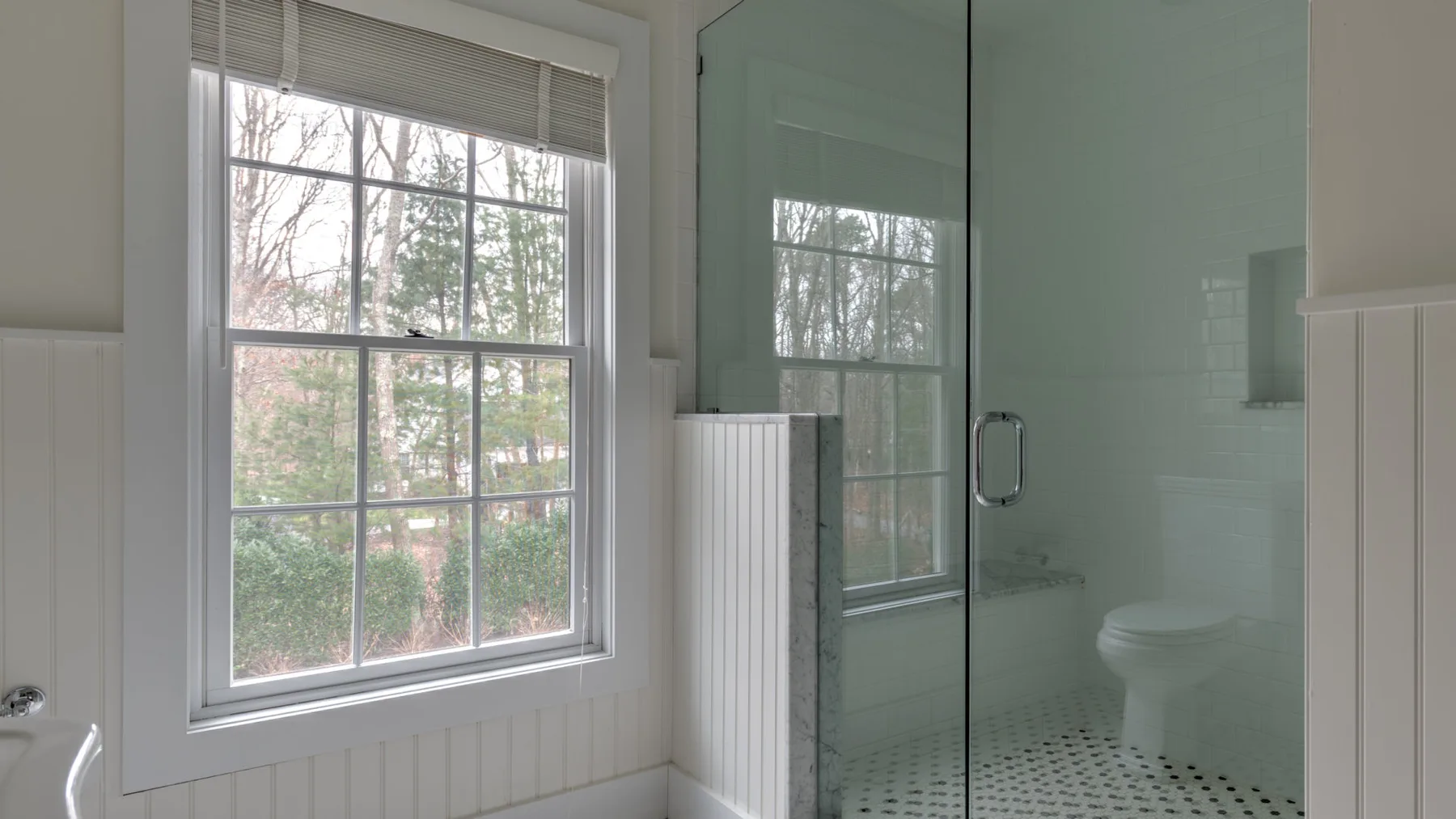 Un baño con ducha de vidrio, inodoro y una ventana grande.