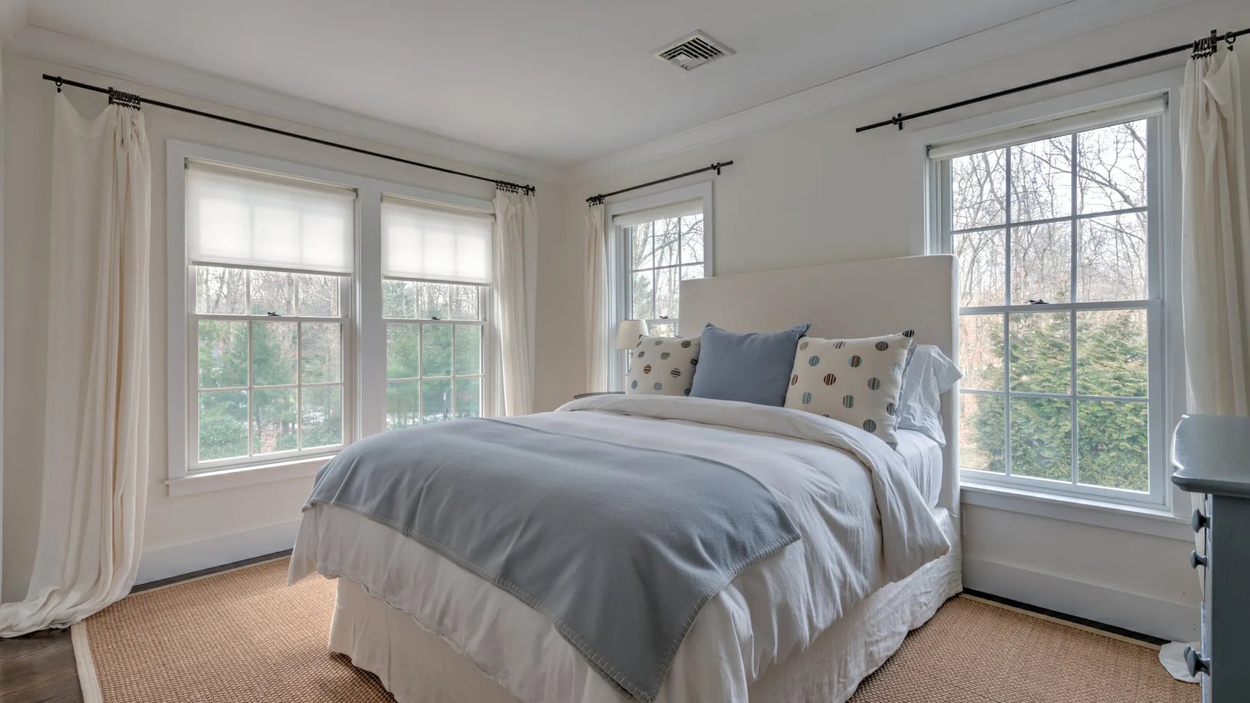Un dormitorio luminoso con una cama tendida junto a varias ventanas grandes.