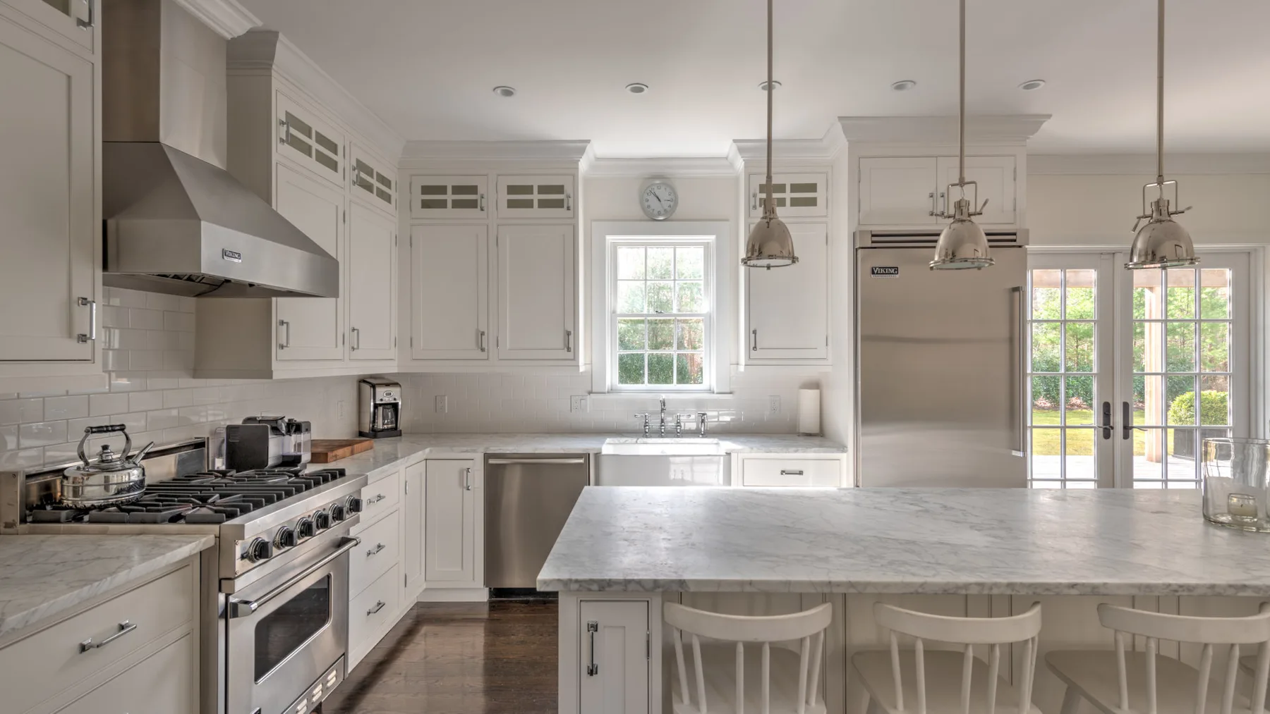 Una cocina luminosa con gabinetes blancos, una isla central y ventanas grandes.