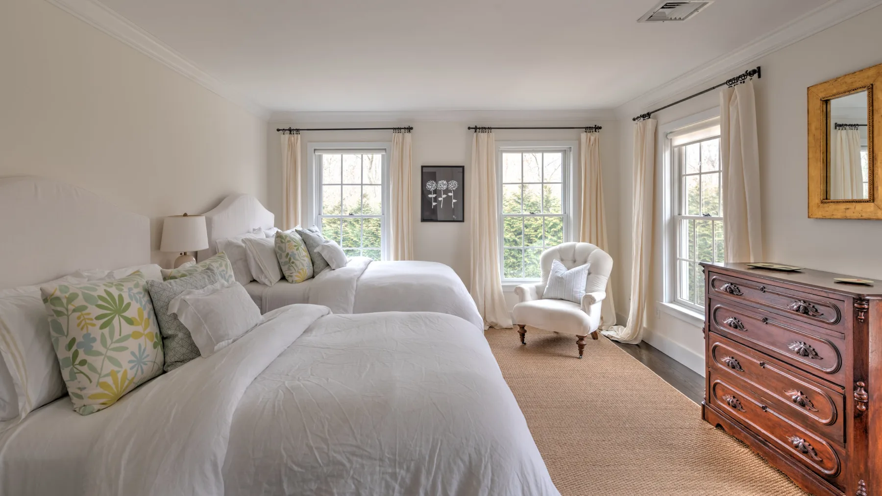 Un dormitorio luminoso con ropa de cama blanca, ventanas grandes y un sillón tapizado.