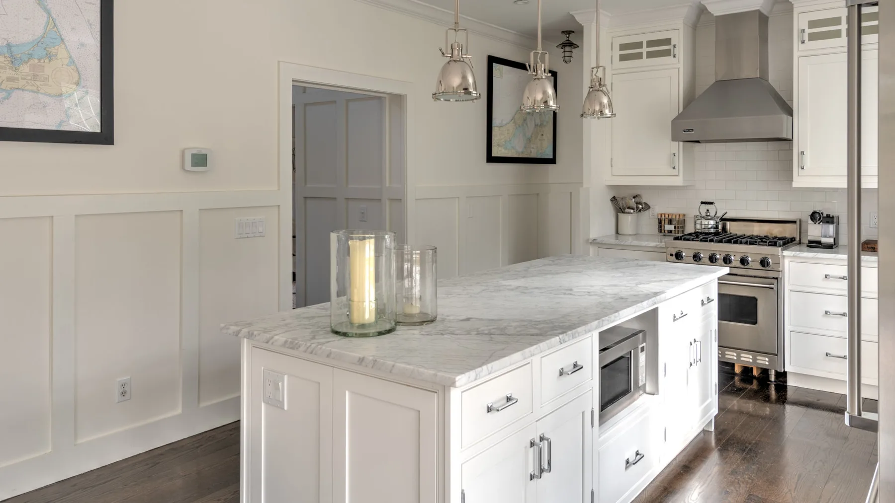 Una cocina luminosa con una isla grande, lámparas colgantes y electrodomésticos de acero inoxidable.