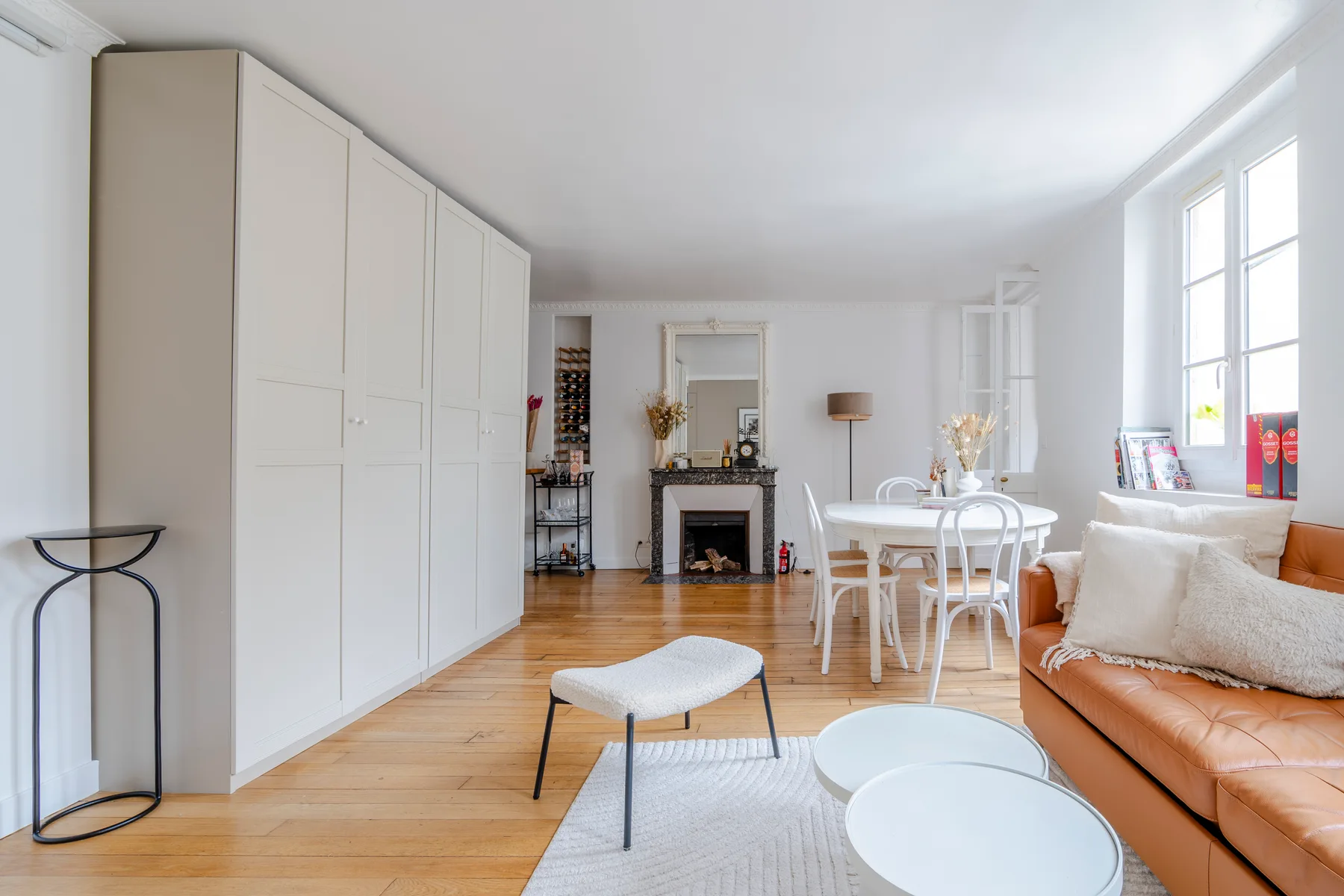 A bright living room with a dining table and seating beside tall windows.