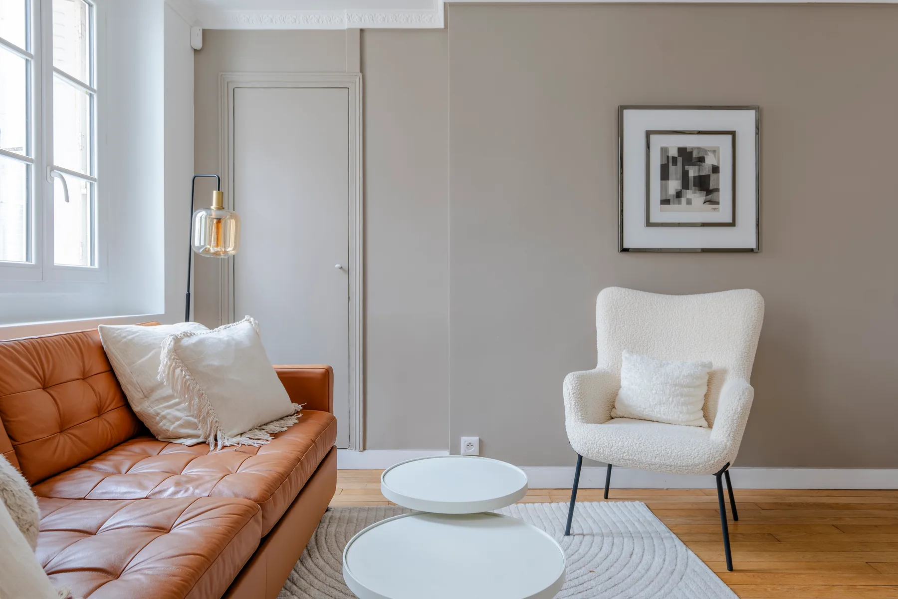 A living room with a brown sofa, a white armchair, and round coffee tables.