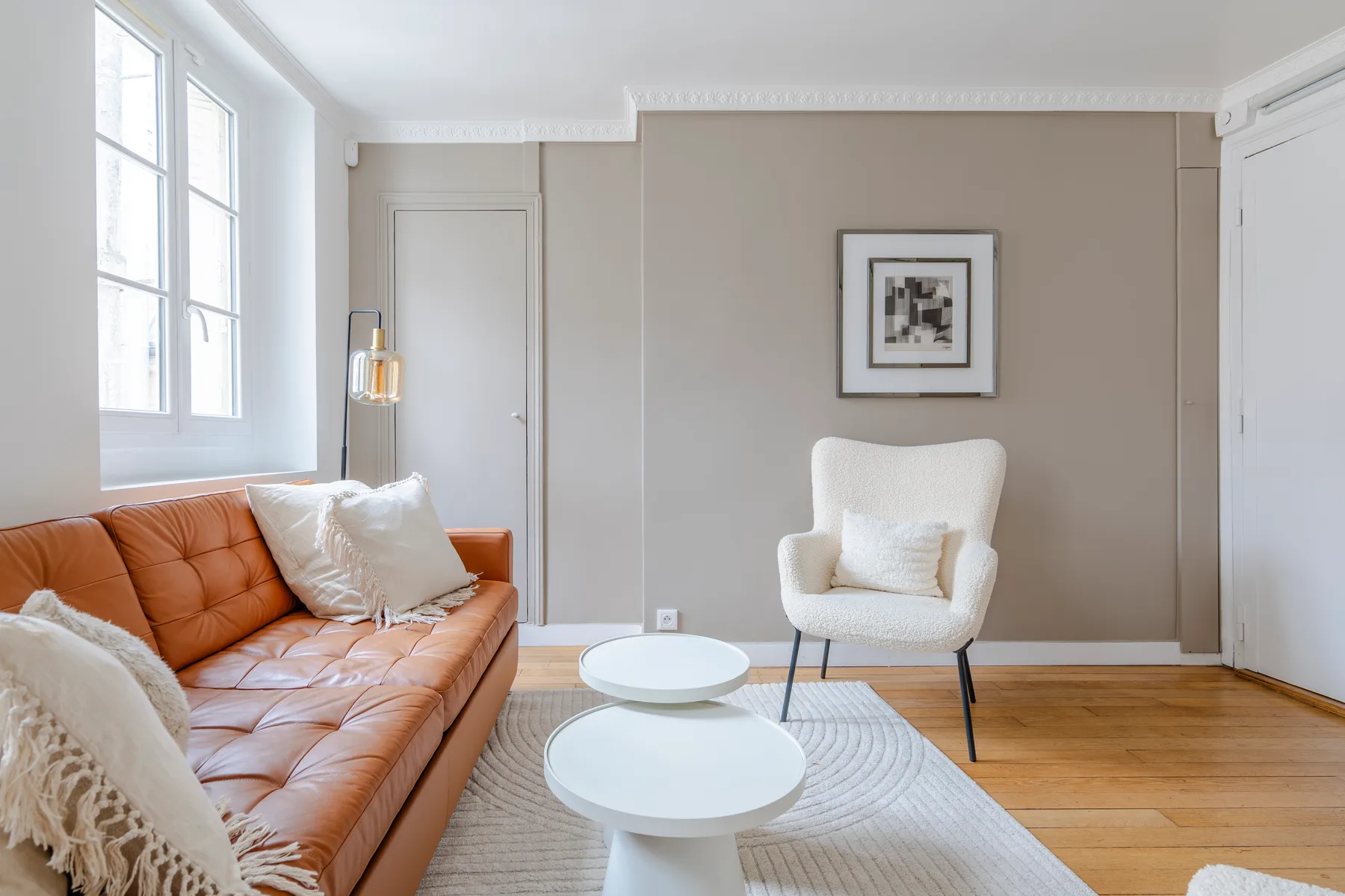 Una sala luminosa con un sofá marrón y un sillón blanco.