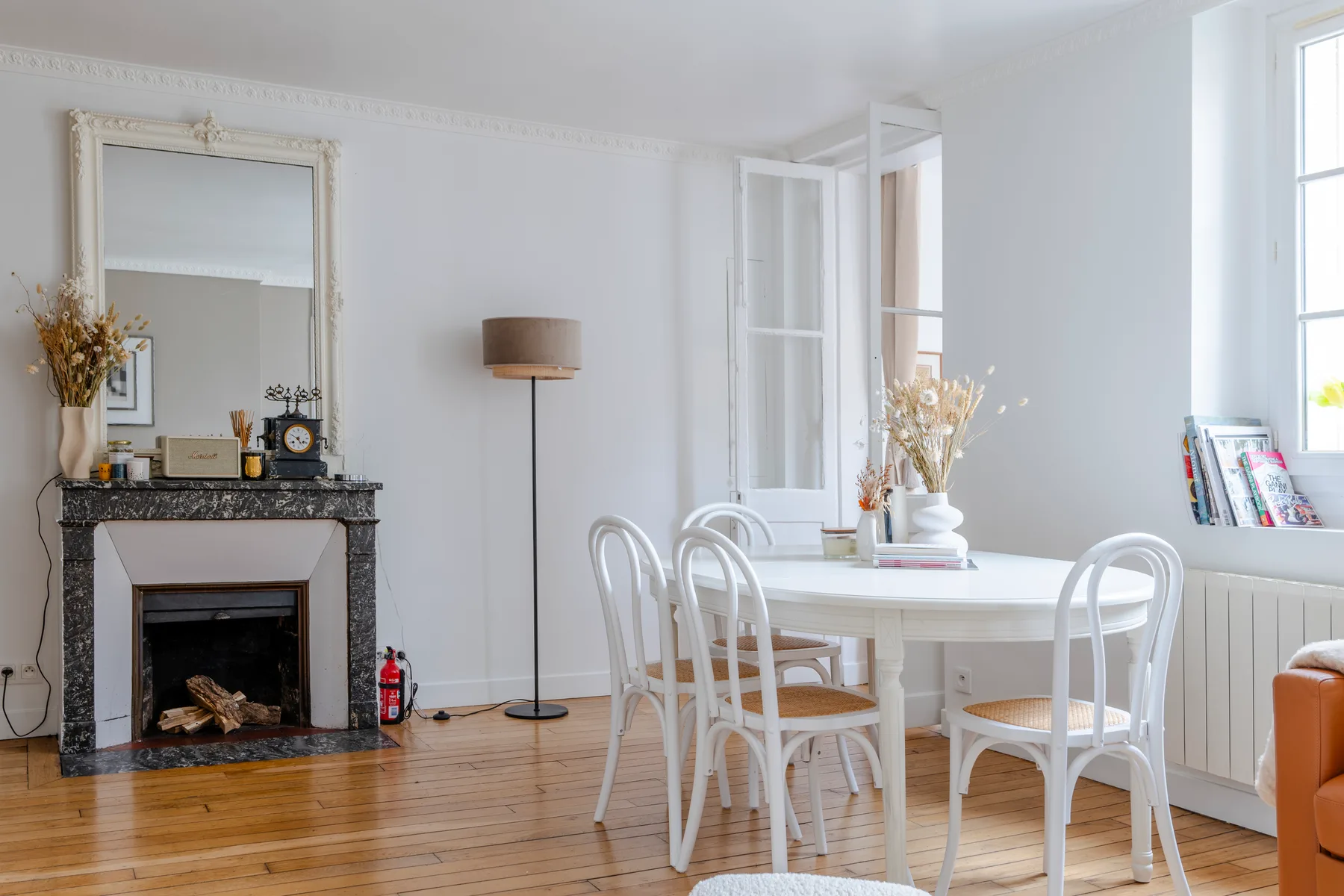 A bright dining area with a white table and seating beside a fireplace.