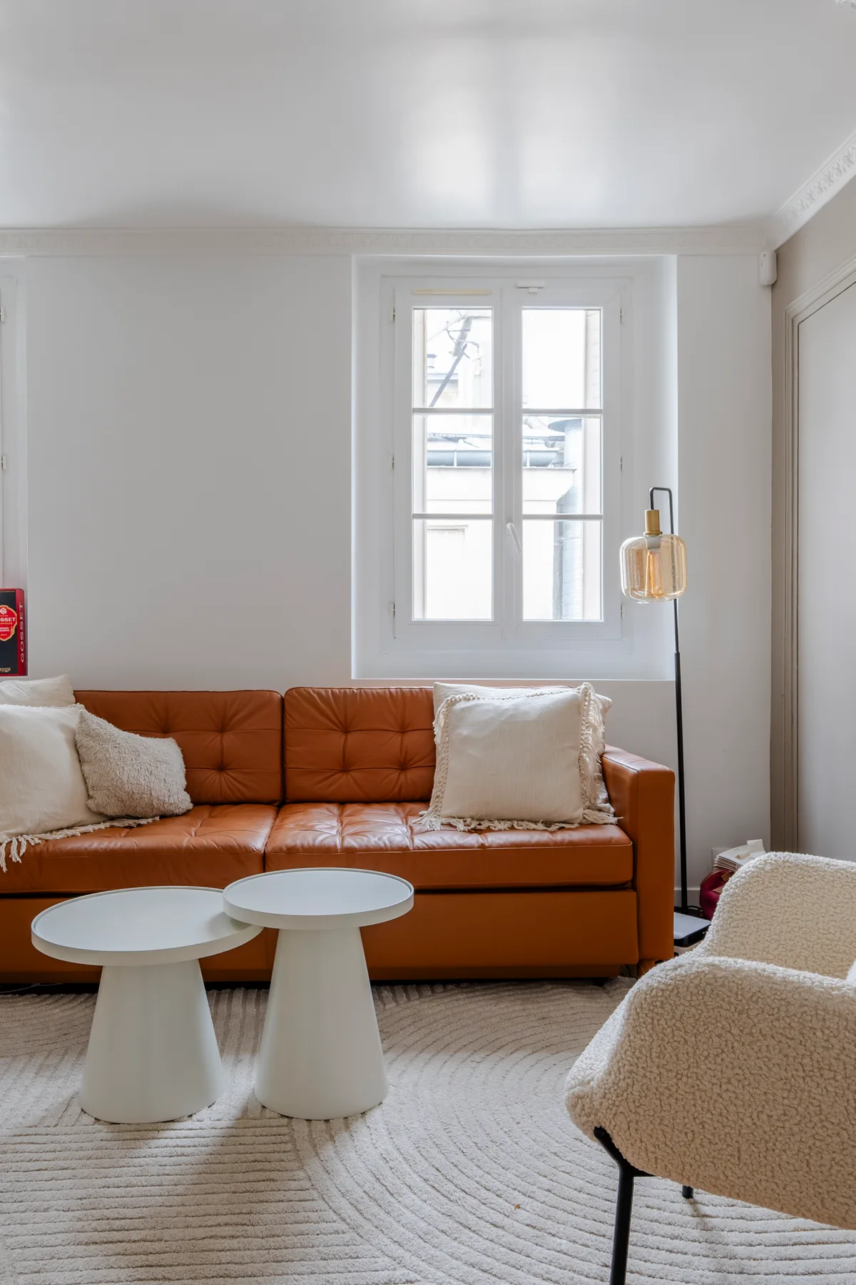 A living room with an orange sofa, two small tables, and a window.