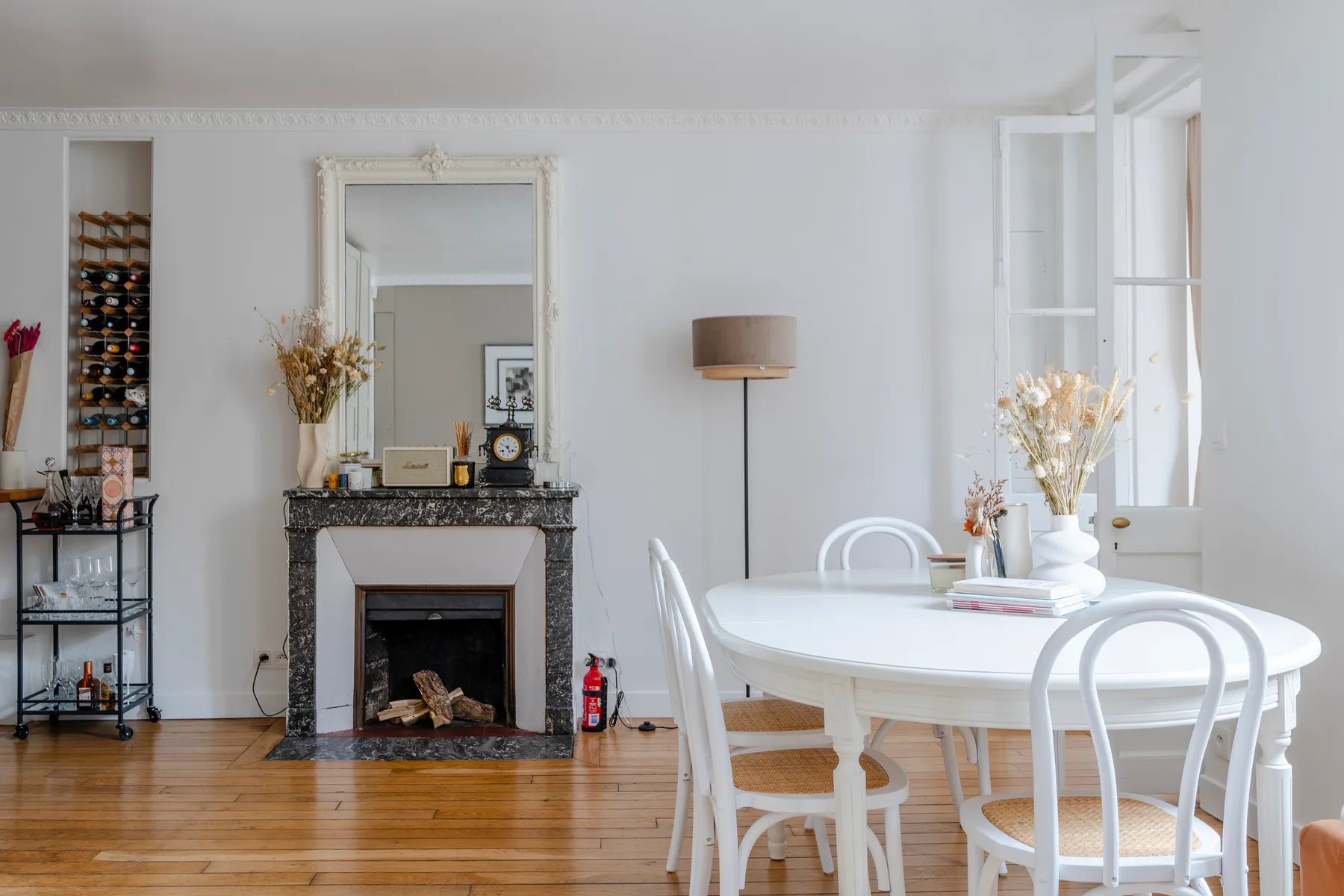 A bright dining area with a white table and chairs beside a fireplace.