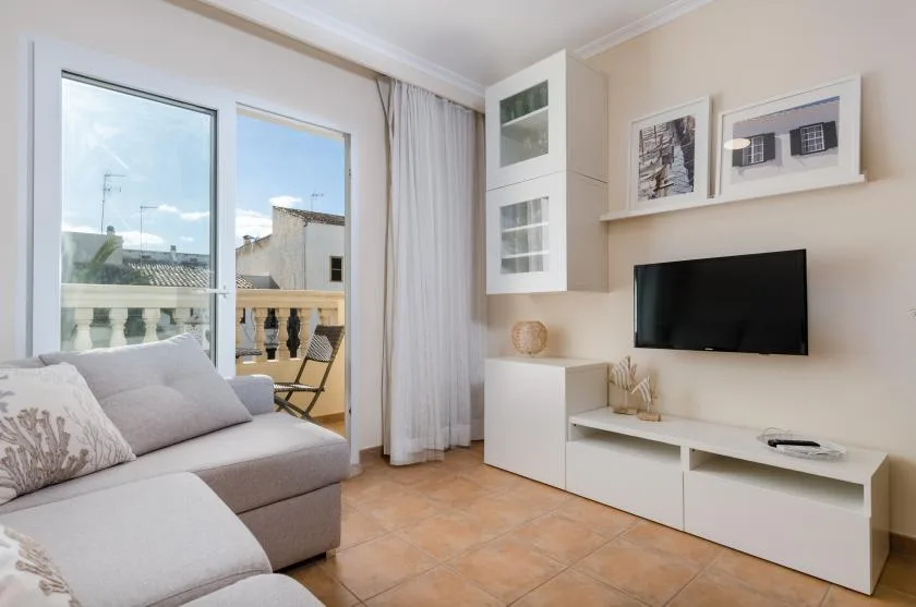 A bright living room with seating beside a large window and a wall-mounted television.
