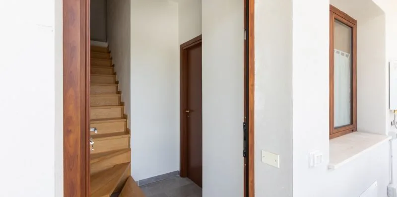 Un pasillo interior con una escalera de madera y una puerta.
