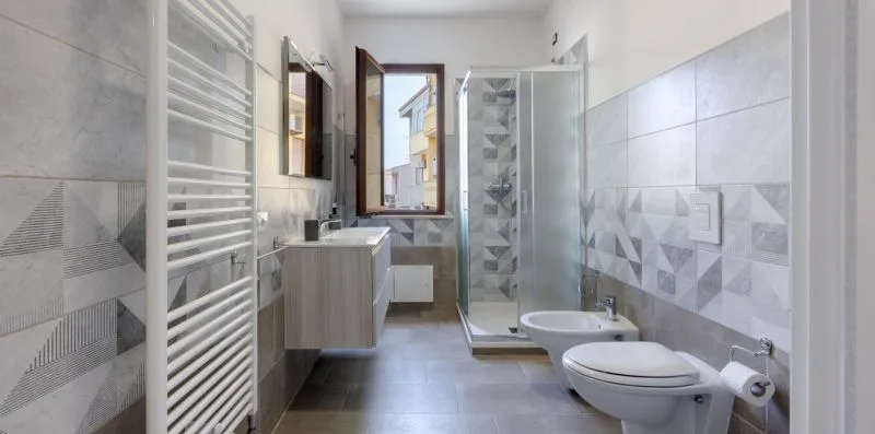 Un baño con azulejos, ducha de vidrio, lavabo y ventana.