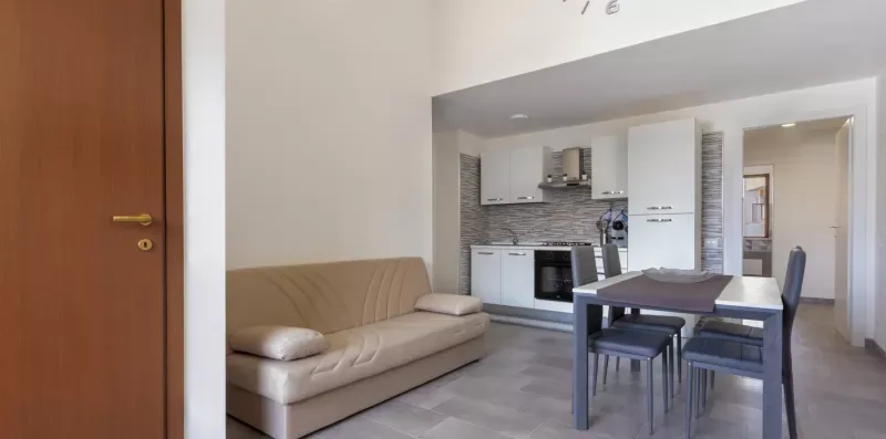 Una sala de estar abierta con sofá, mesa de comedor y cocina compacta.