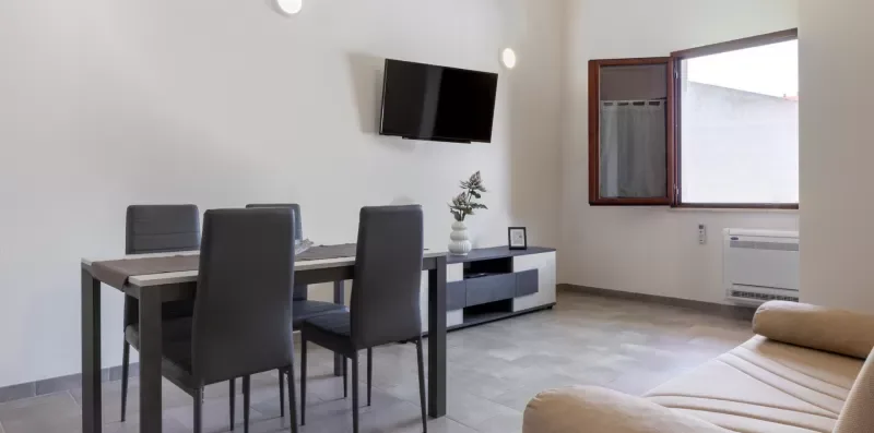 Zona de comedor y estar con una mesa, asientos y un televisor montado en la pared.