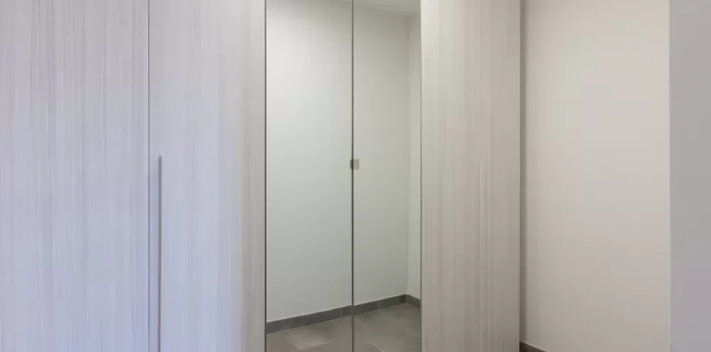 Un pasillo interior luminoso con paredes claras y una puerta de armario con espejo.