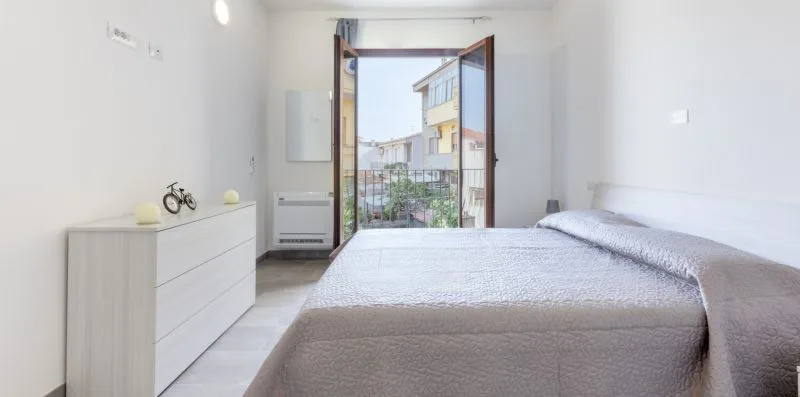 Un dormitorio luminoso con una cama y la puerta del balcón abierta.