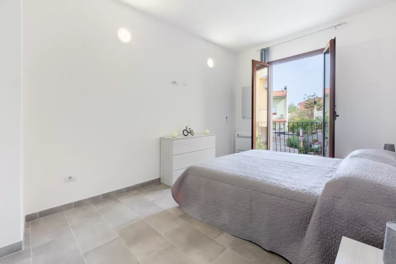 Un dormitorio luminoso con una cama y la puerta del balcón abierta.