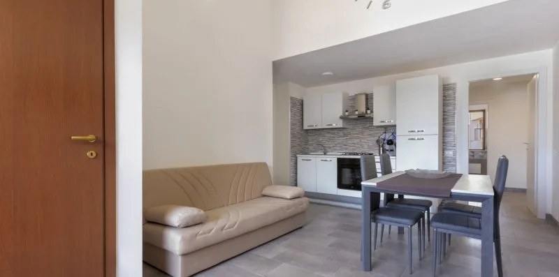 Una sala de estar y comedor con sofá beige, mesa y cocina.