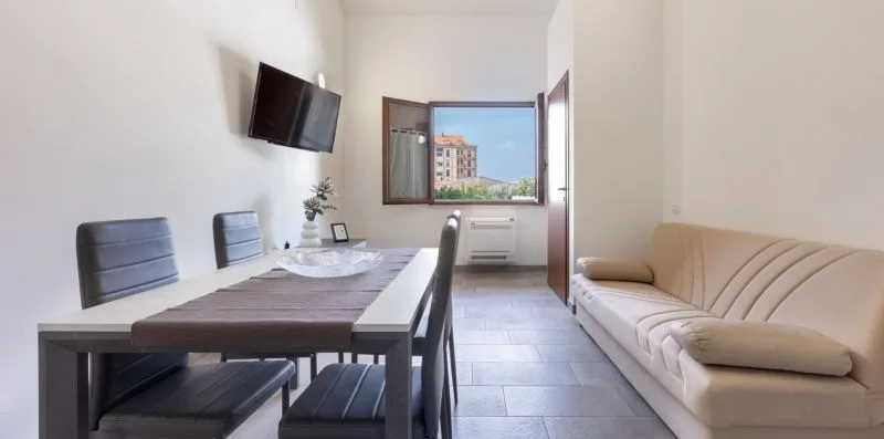 Comedor con mesa y asientos junto a un sofá y una ventana abierta.