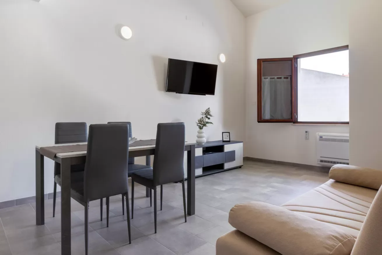 Una luminosa sala de estar y comedor con mesa, asientos y un televisor en la pared.