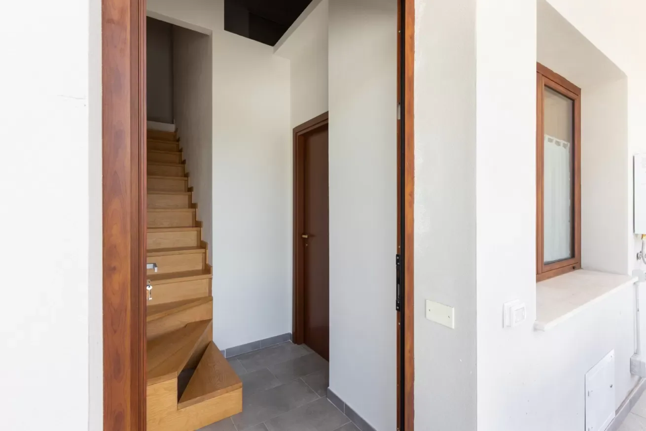 Un pasillo interior con una escalera de madera y una puerta cerrada.