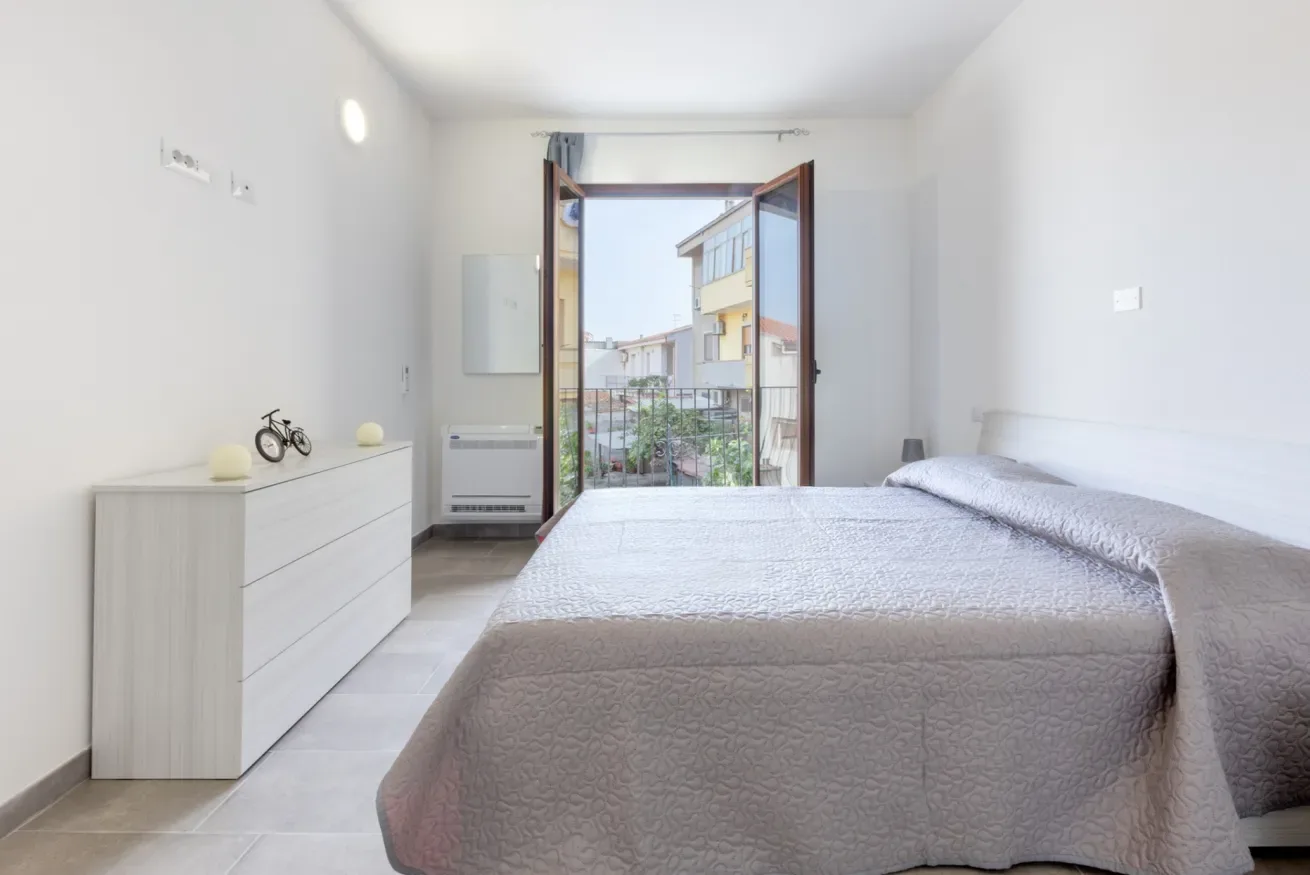 Un dormitorio luminoso con una cama frente a una puerta abierta al balcón.