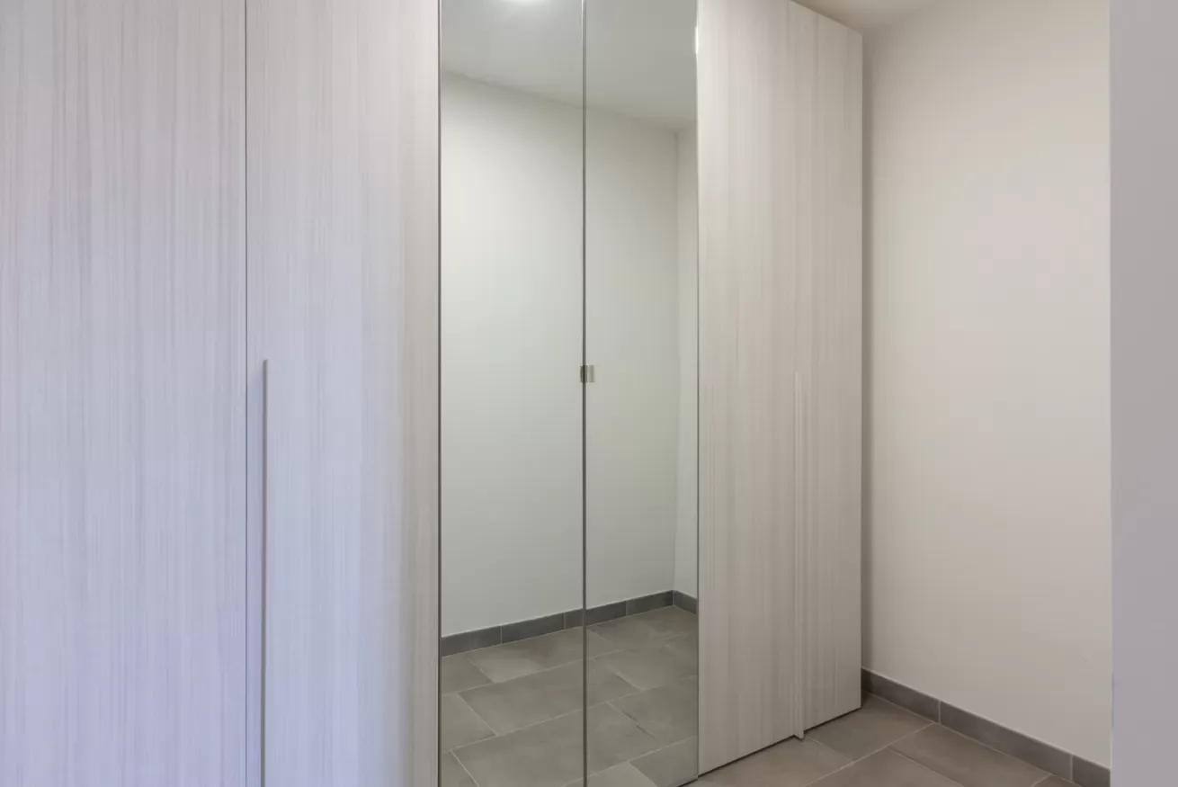 Un armario con espejo está junto a un suelo de baldosas en un interior luminoso.