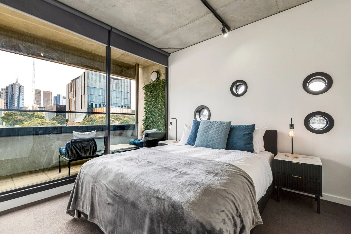 Descansa en el dormitorio principal, que cuenta con una cama queen vestida con varias capas de ropa de cama, mantas suaves y acceso directo al balcón con vistas del perfil urbano.