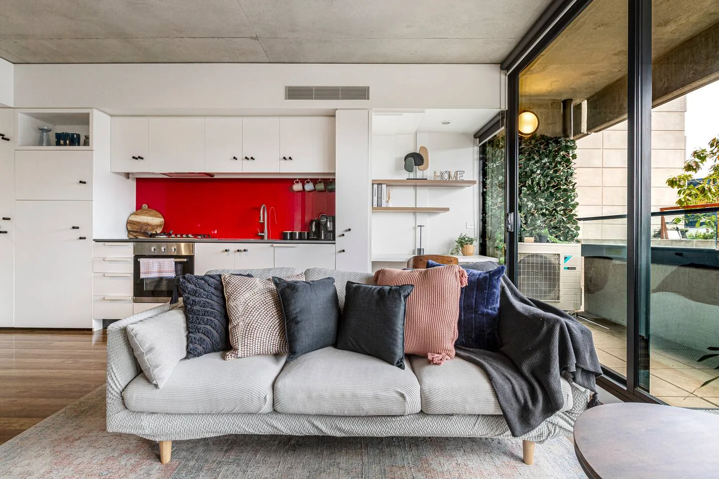 Sala de estar con un sofá frente a una cocina con salpicadero rojo intenso.