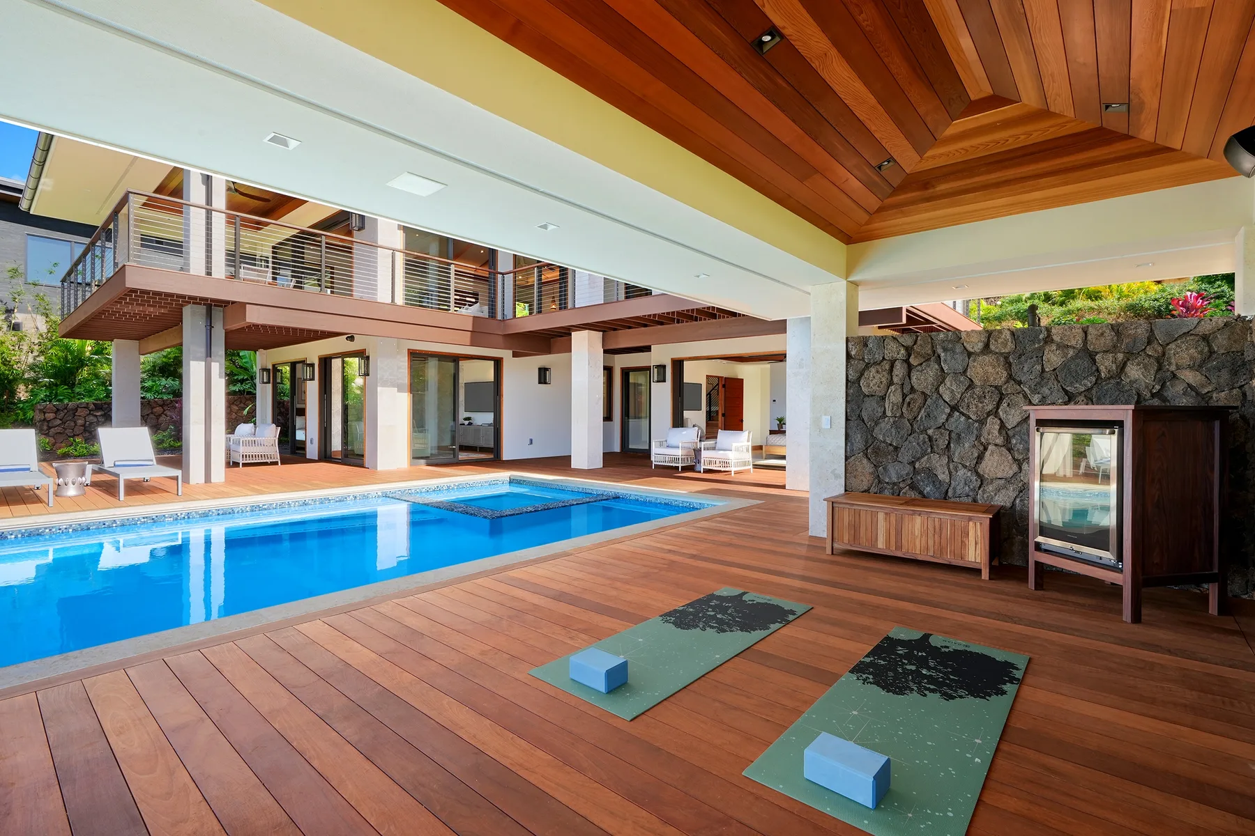 Un patio cubierto junto a la piscina, con una tarima de madera y dos esterillas de ejercicio.