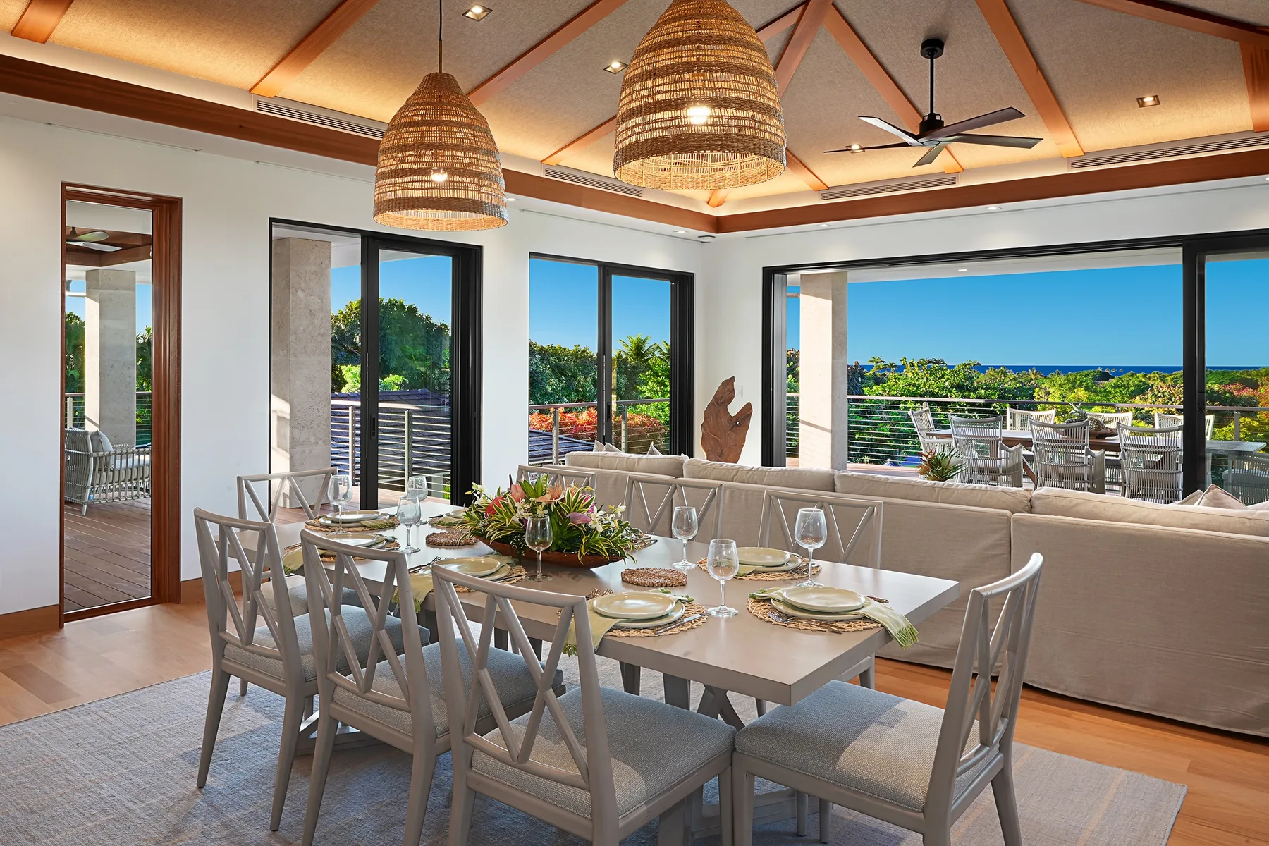 Un comedor luminoso con una mesa larga junto a grandes ventanales con vistas a la vegetación y el mar.