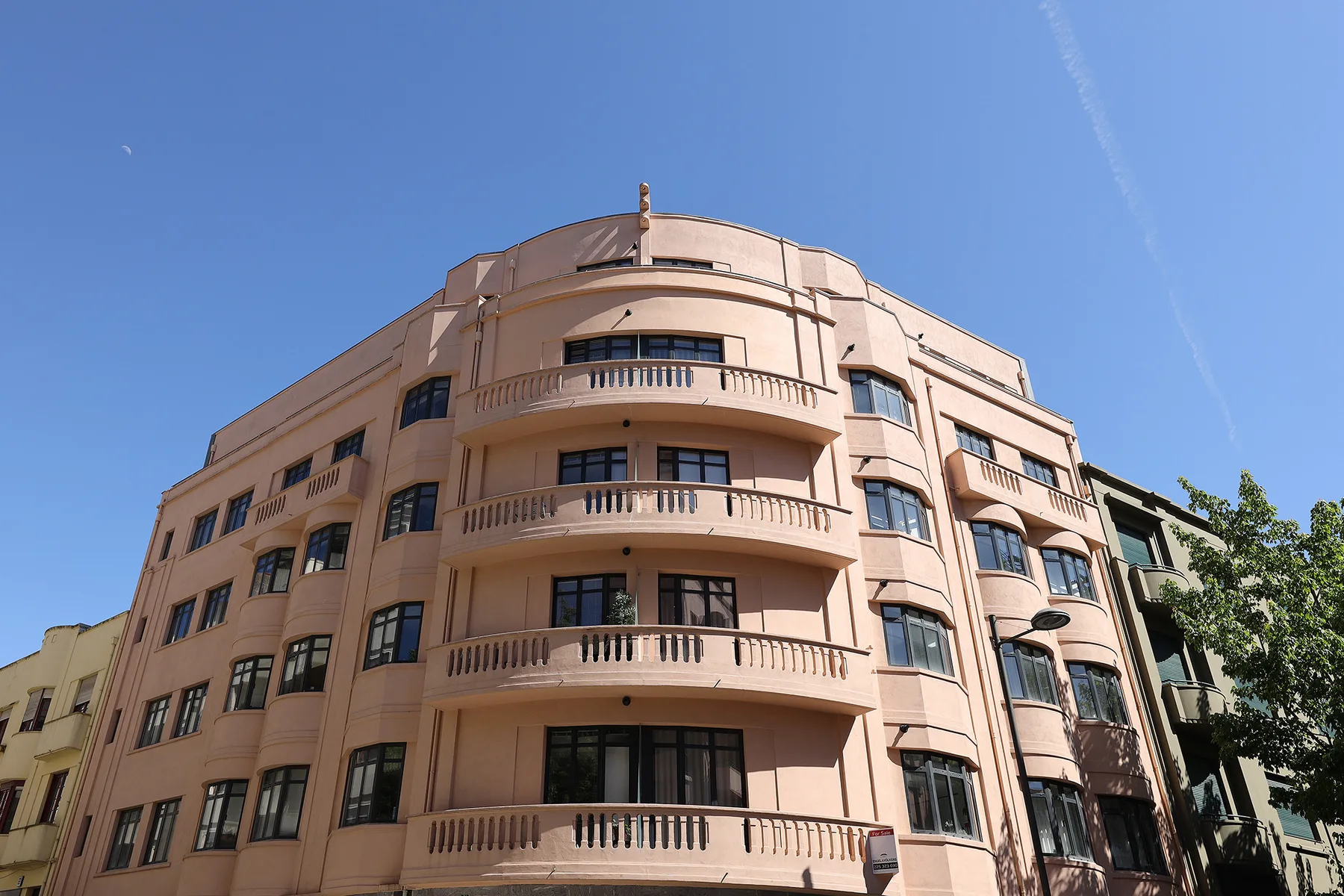 A curved pink apartment building rises against a clear blue sky.