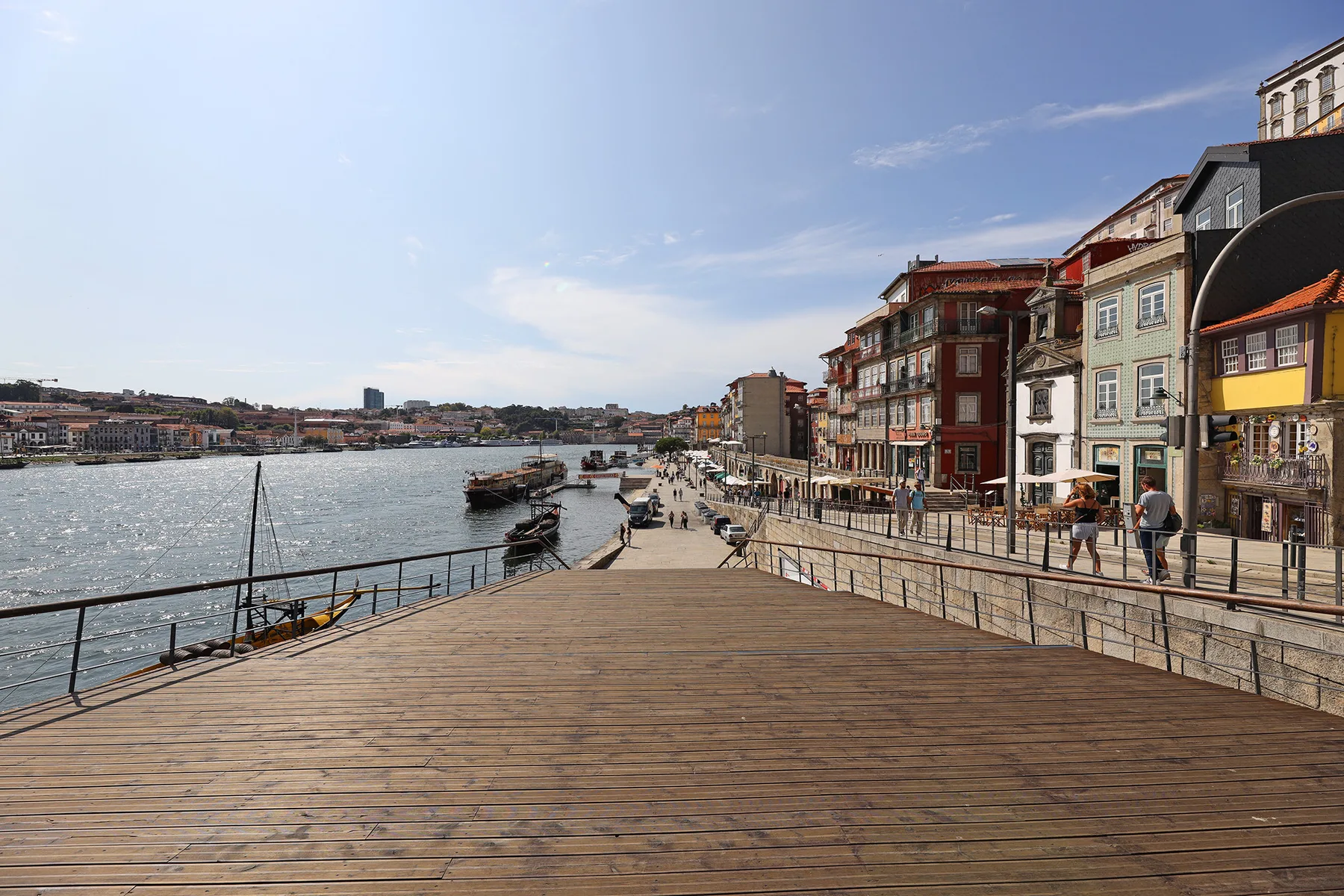 A wooden riverside promenade runs alongside the water and colorful waterfront buildings.
