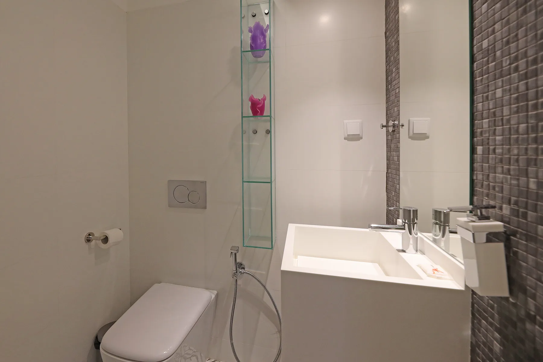 A bathroom with a toilet, sink, and glass wall shelving.