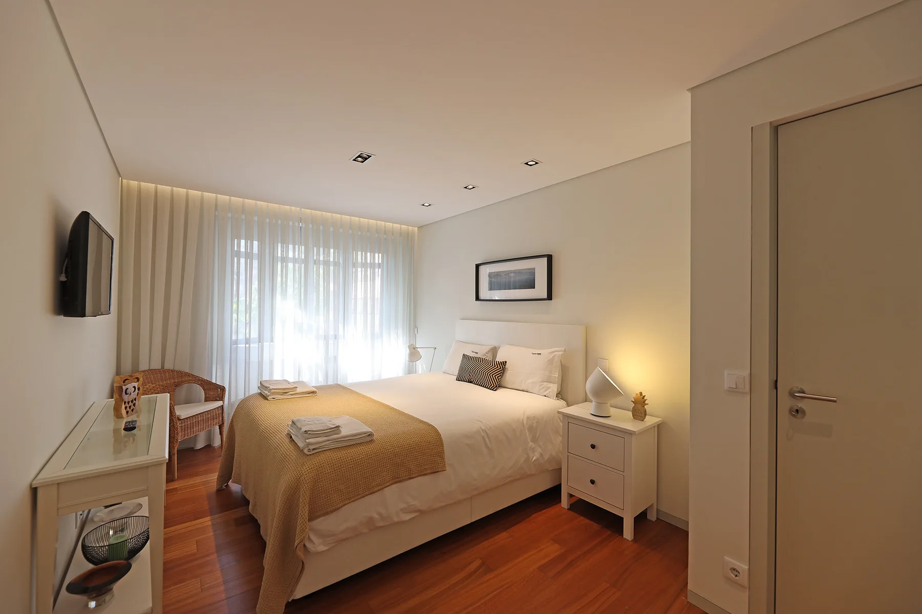A bedroom with a double bed, bedside tables, and a curtained window.