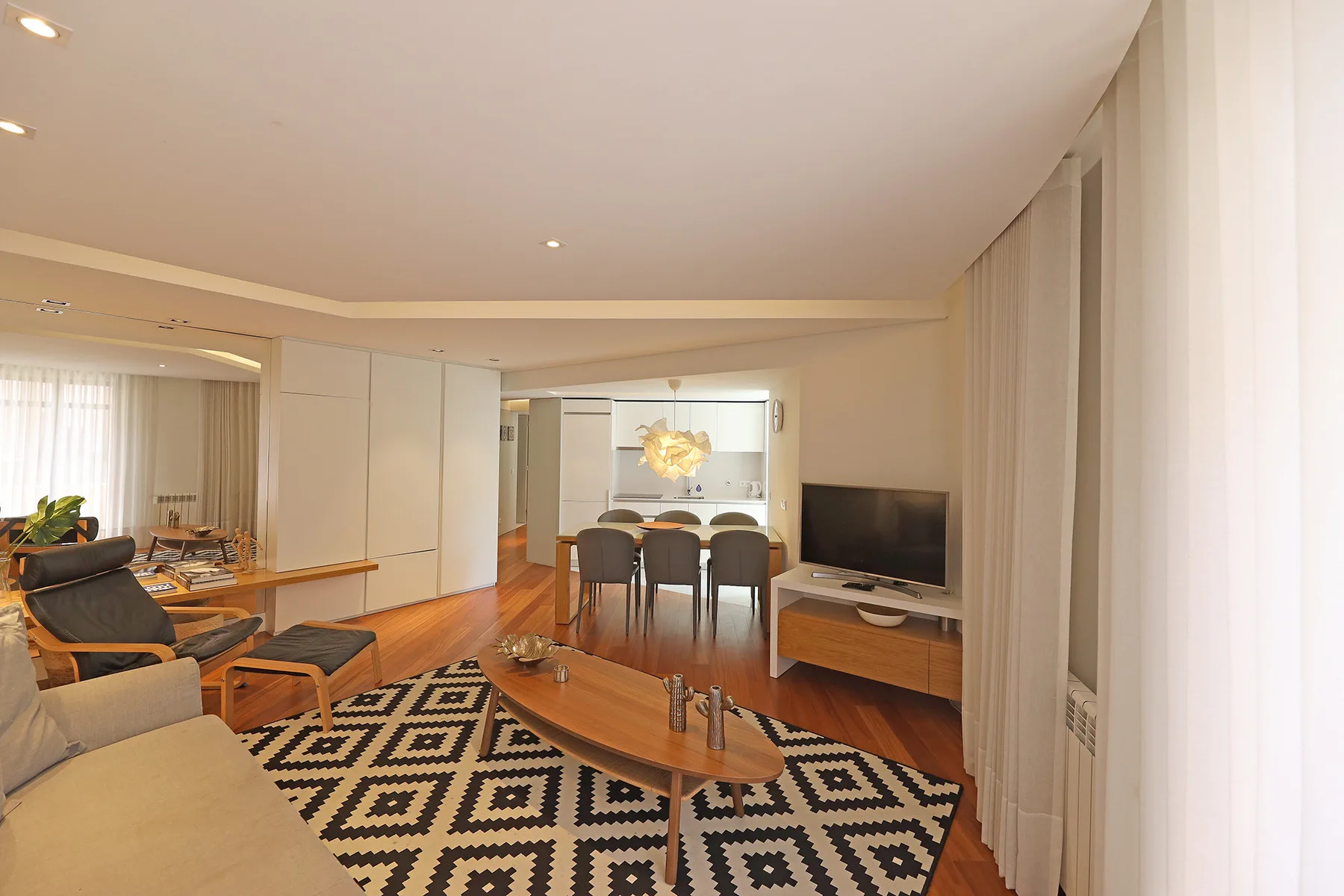 A living and dining area with a patterned rug and a television.