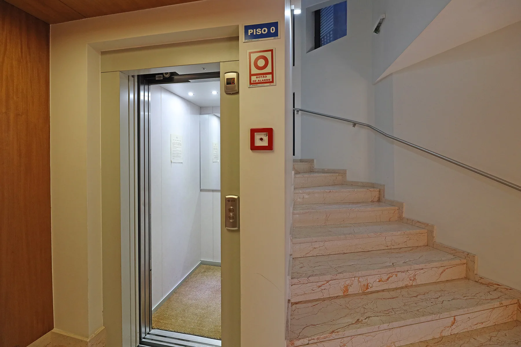 An elevator entrance beside a staircase in an indoor building hallway.