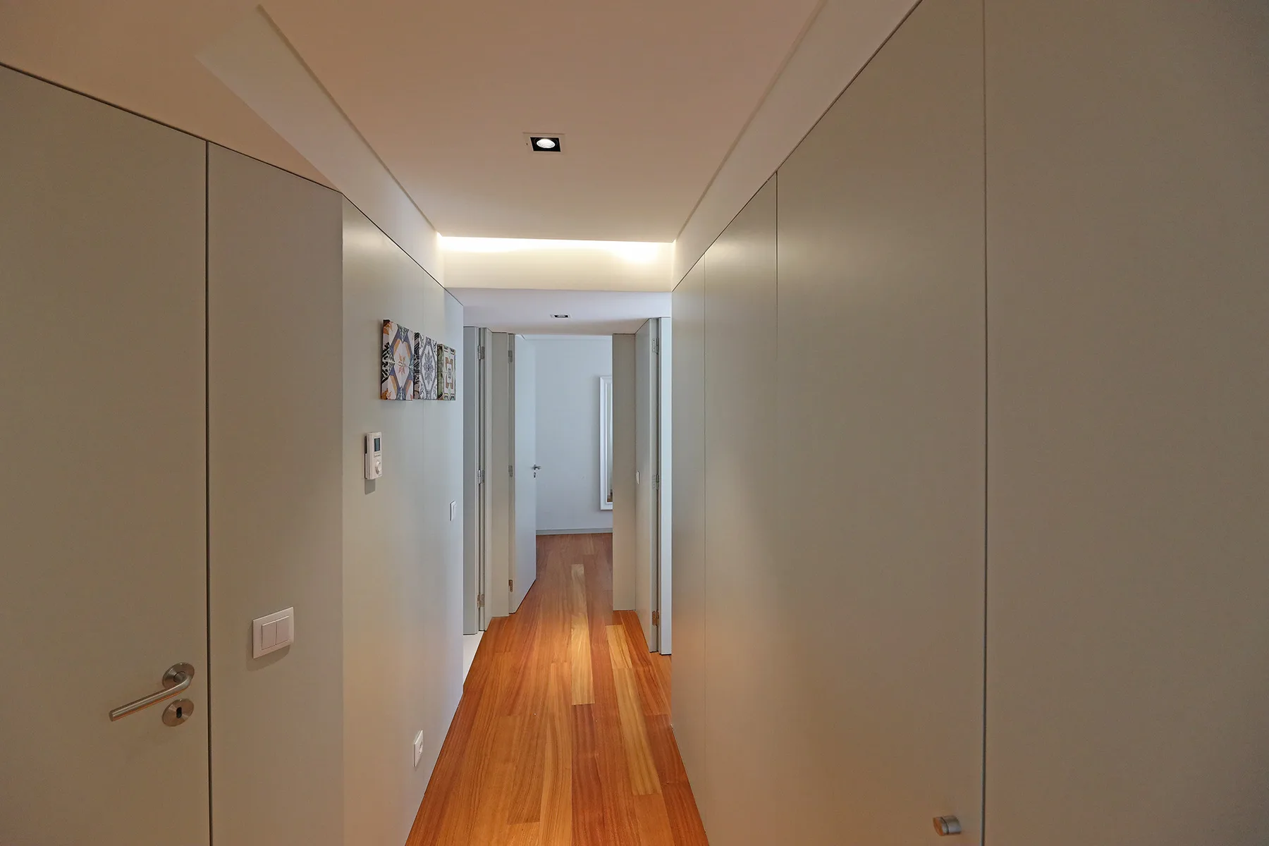 A hallway with wood flooring leads toward a bright room.