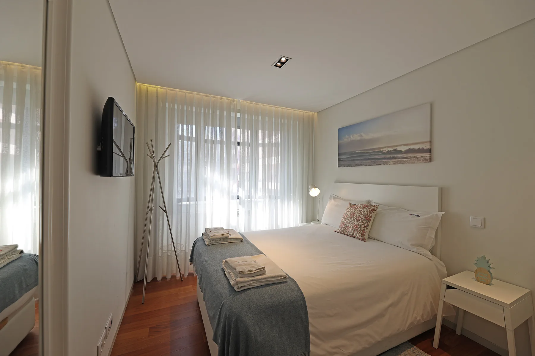 A bright bedroom with a neatly made bed and sheer curtains.