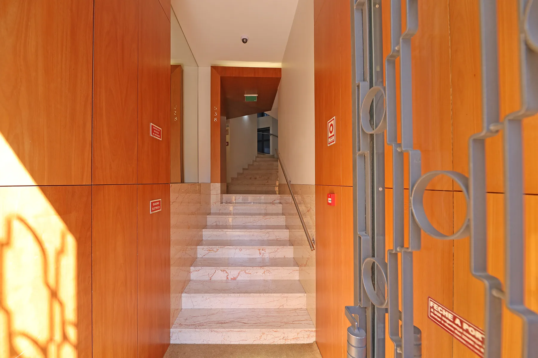 A sunlit building entrance opens onto a marble staircase with metal railings.