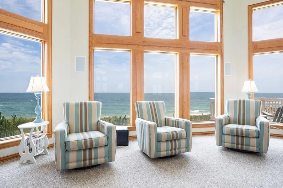 Una luminosa zona de estar con sillones a rayas frente a grandes ventanas con vistas al mar.