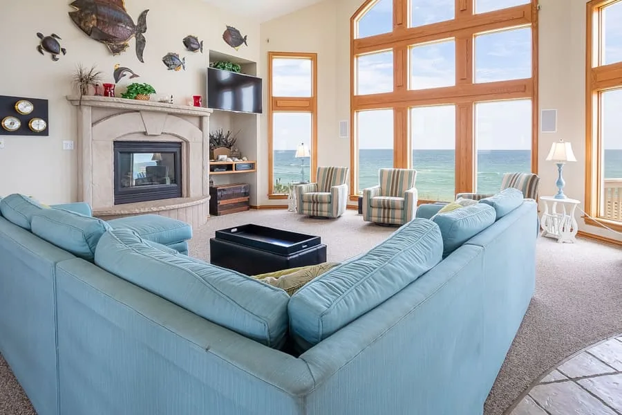 Una sala luminosa con asientos frente a una chimenea y ventanas con vistas al mar.