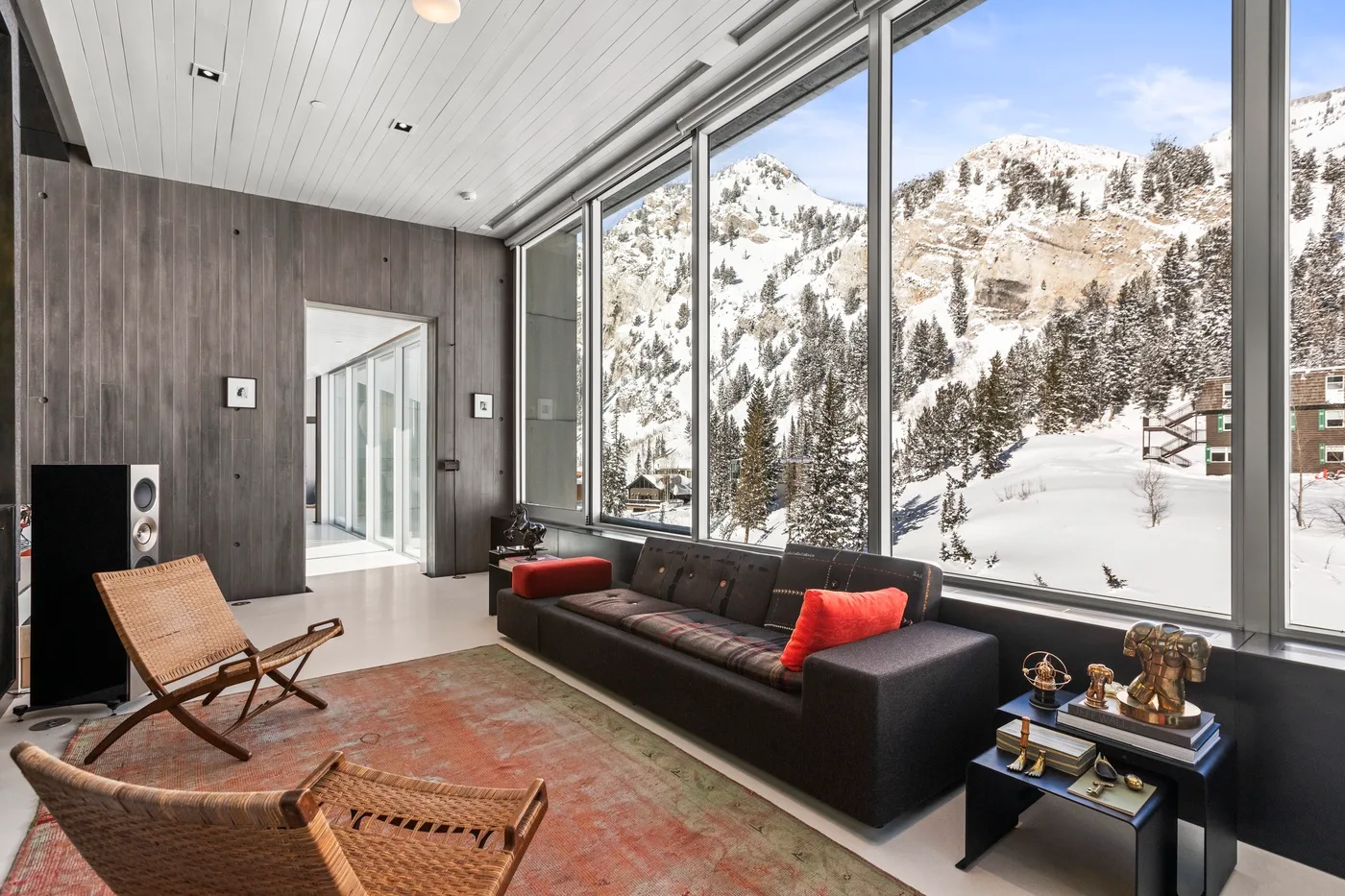 A modern living room with seating beside large windows overlooking a snowy mountain landscape.