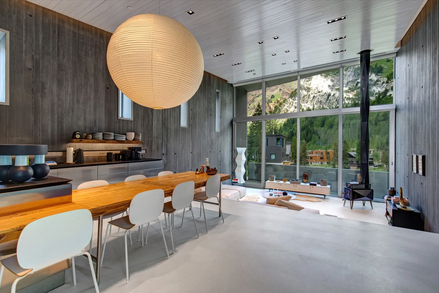 A modern open-plan living and dining area with a long wooden table and tall windows.