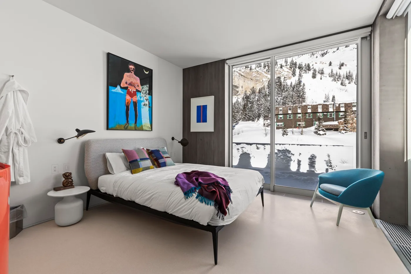 A bedroom with a bed beside large windows overlooking a snowy landscape.