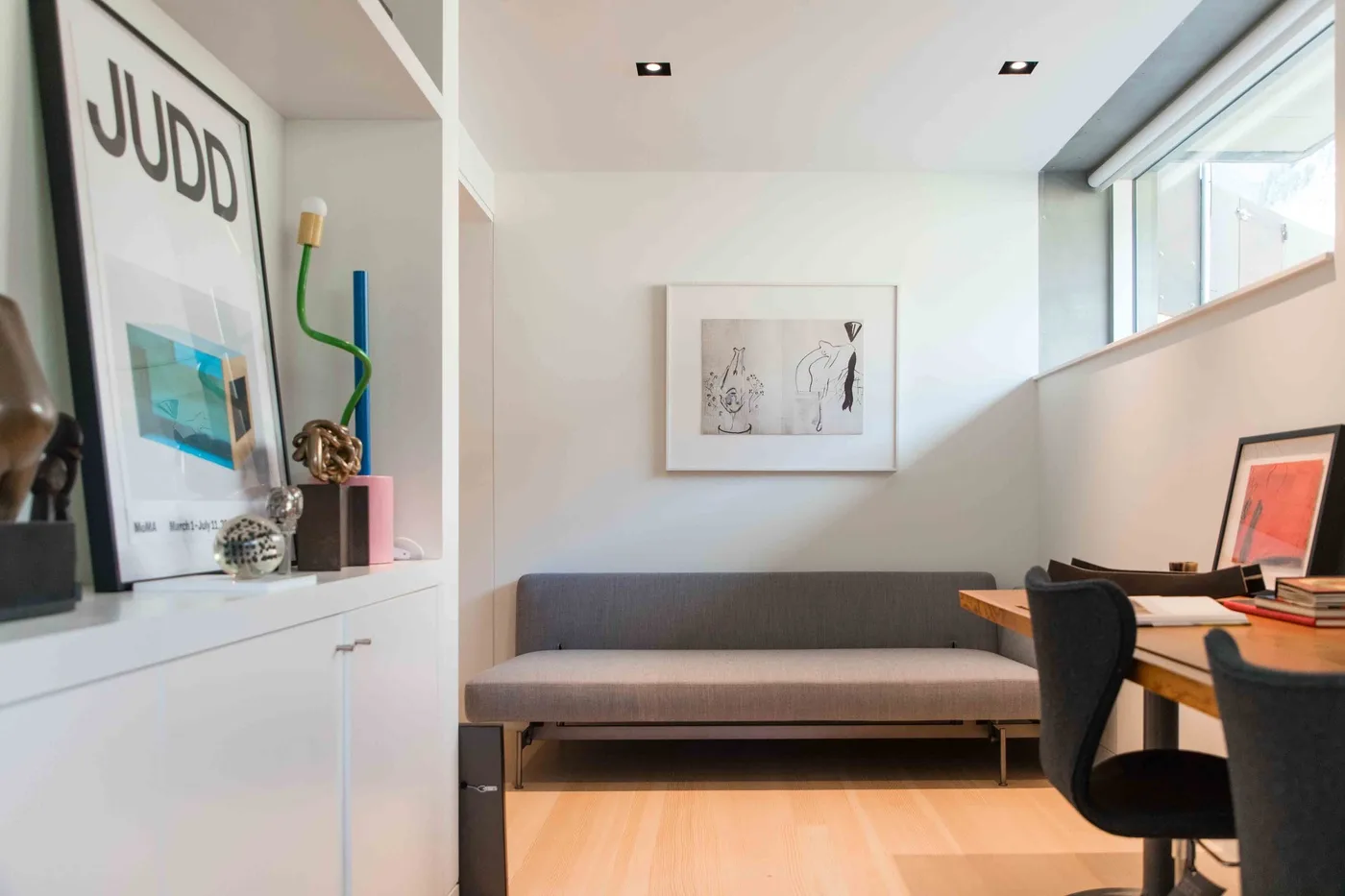 A bright sitting area with a gray sofa, a desk, and built-in shelving.