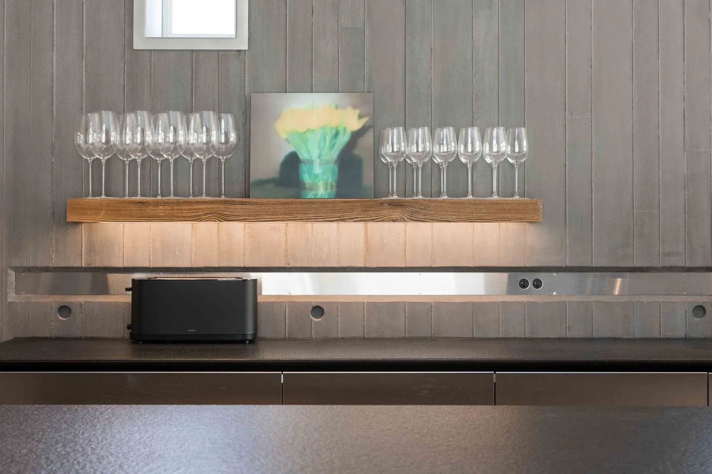 A modern kitchen counter with a row of wine glasses and a small artwork.