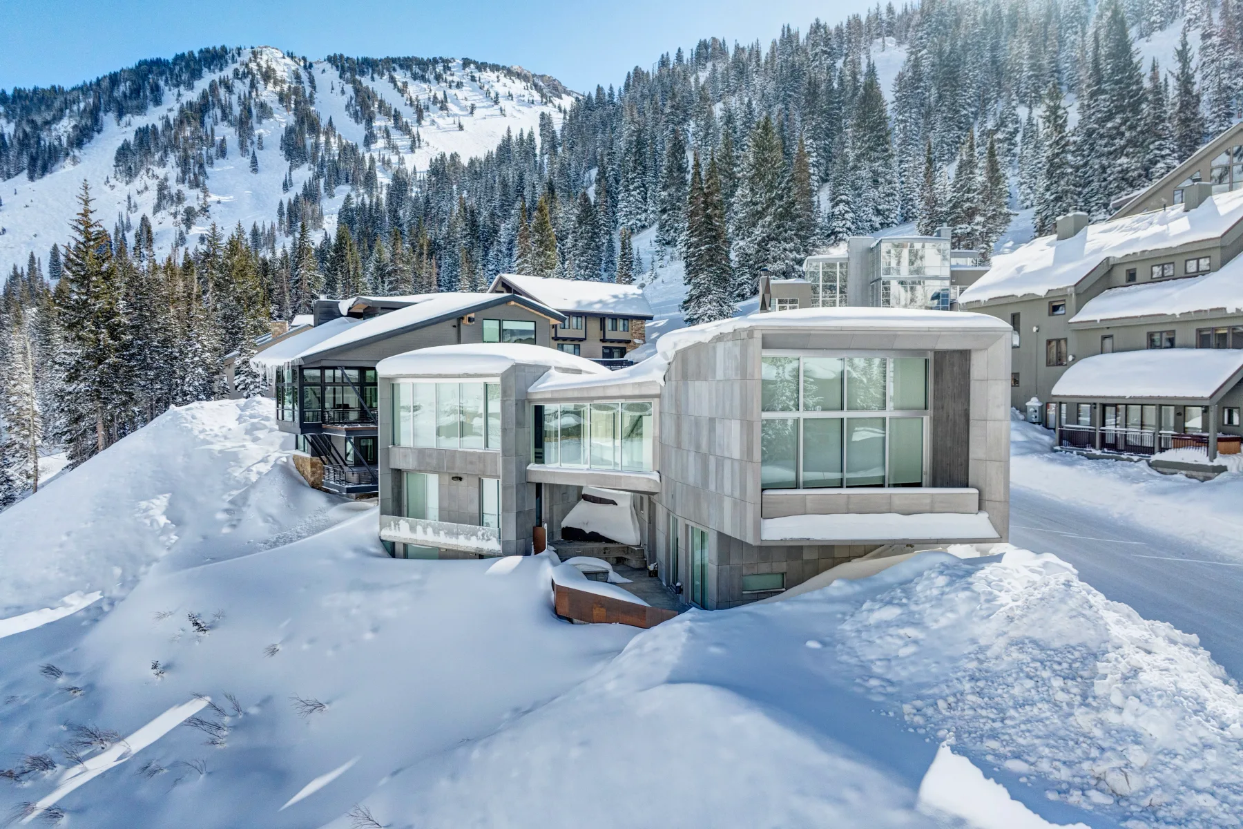 Modern buildings sit amid deep snow, with a forested mountain rising behind them.