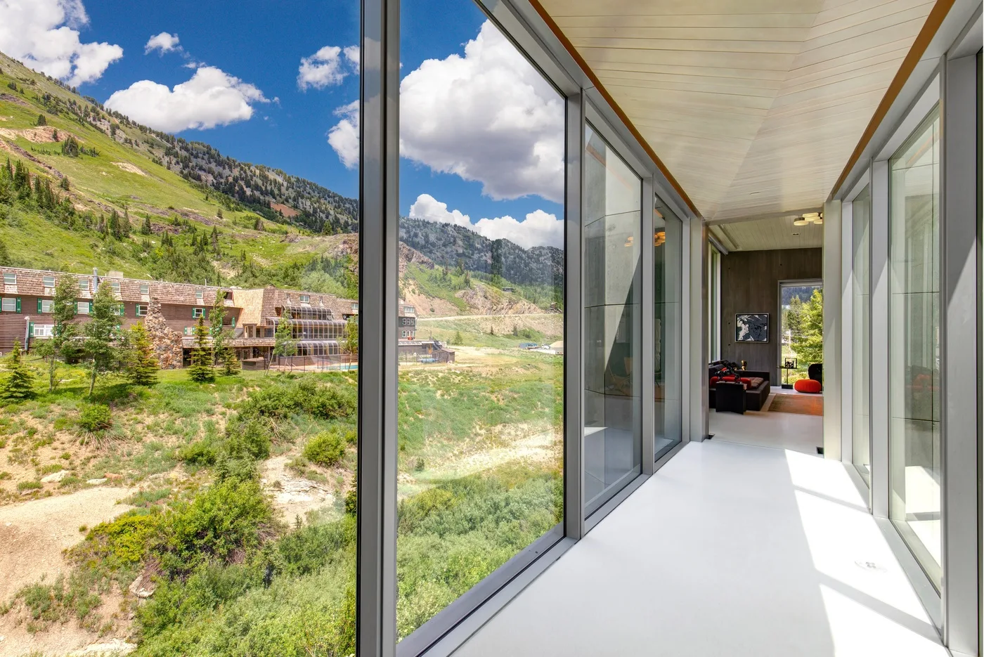 A bright glass-walled corridor opens onto views of green hills and buildings.